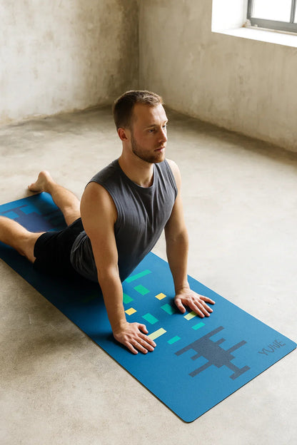 Man practicing yoga on a blue mat with colorful designs in a room with a window.
