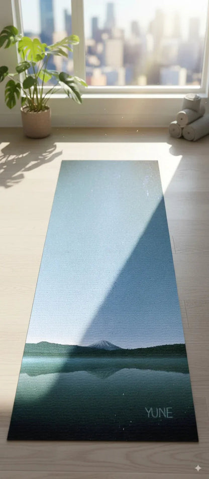 Yoga mat with mountain design on a wooden floor next to a window with plants.