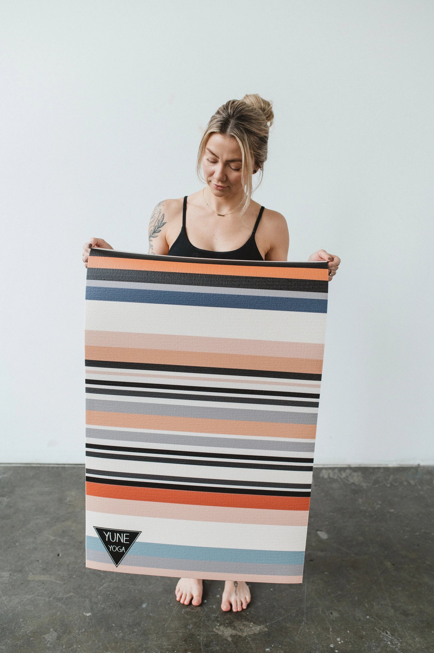 Woman holding a colorful striped yoga mat with a plain background