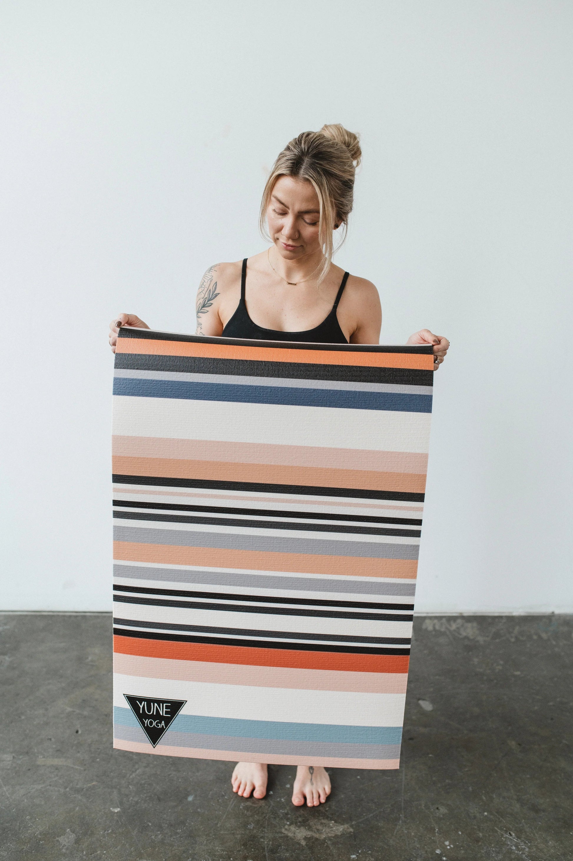 Woman holding a colorful striped yoga mat with a plain background