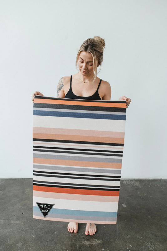 Woman holding a colorful striped yoga mat with a plain background