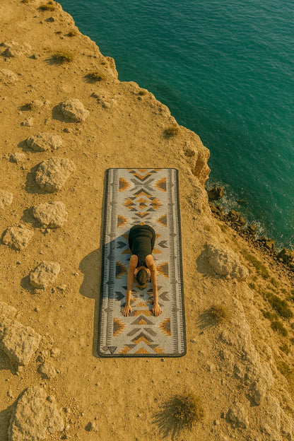 Person sitting on a patterned mat by a body of water