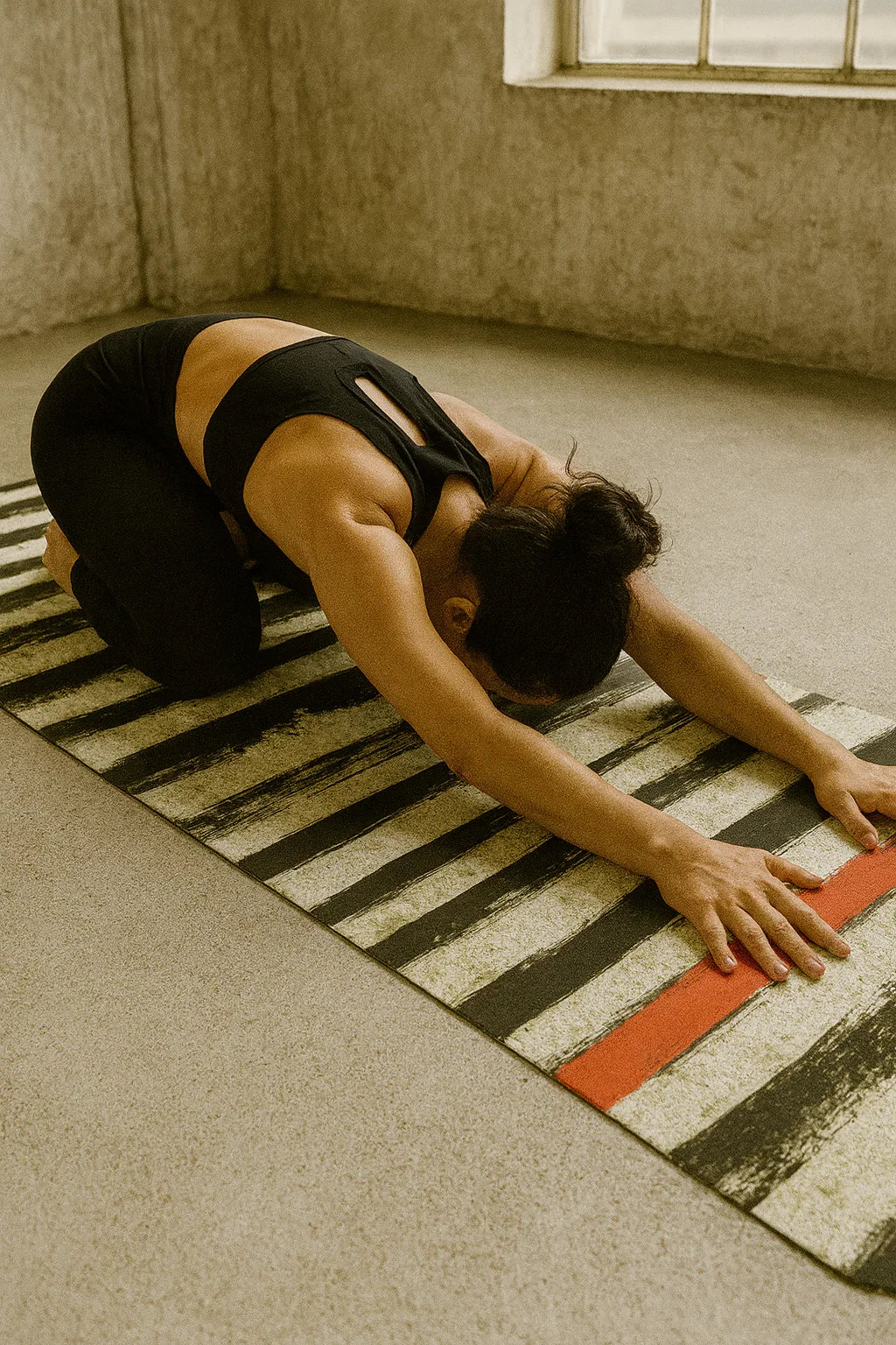 Person stretching on a striped mat in a room with a window.