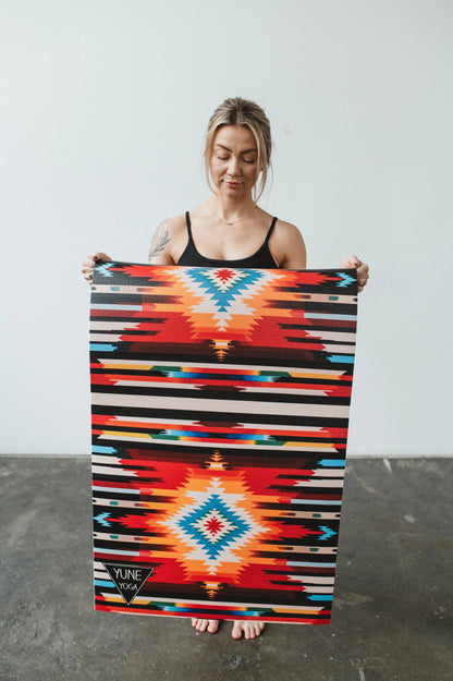 Woman holding a colorful patterned blanket with a geometric design.