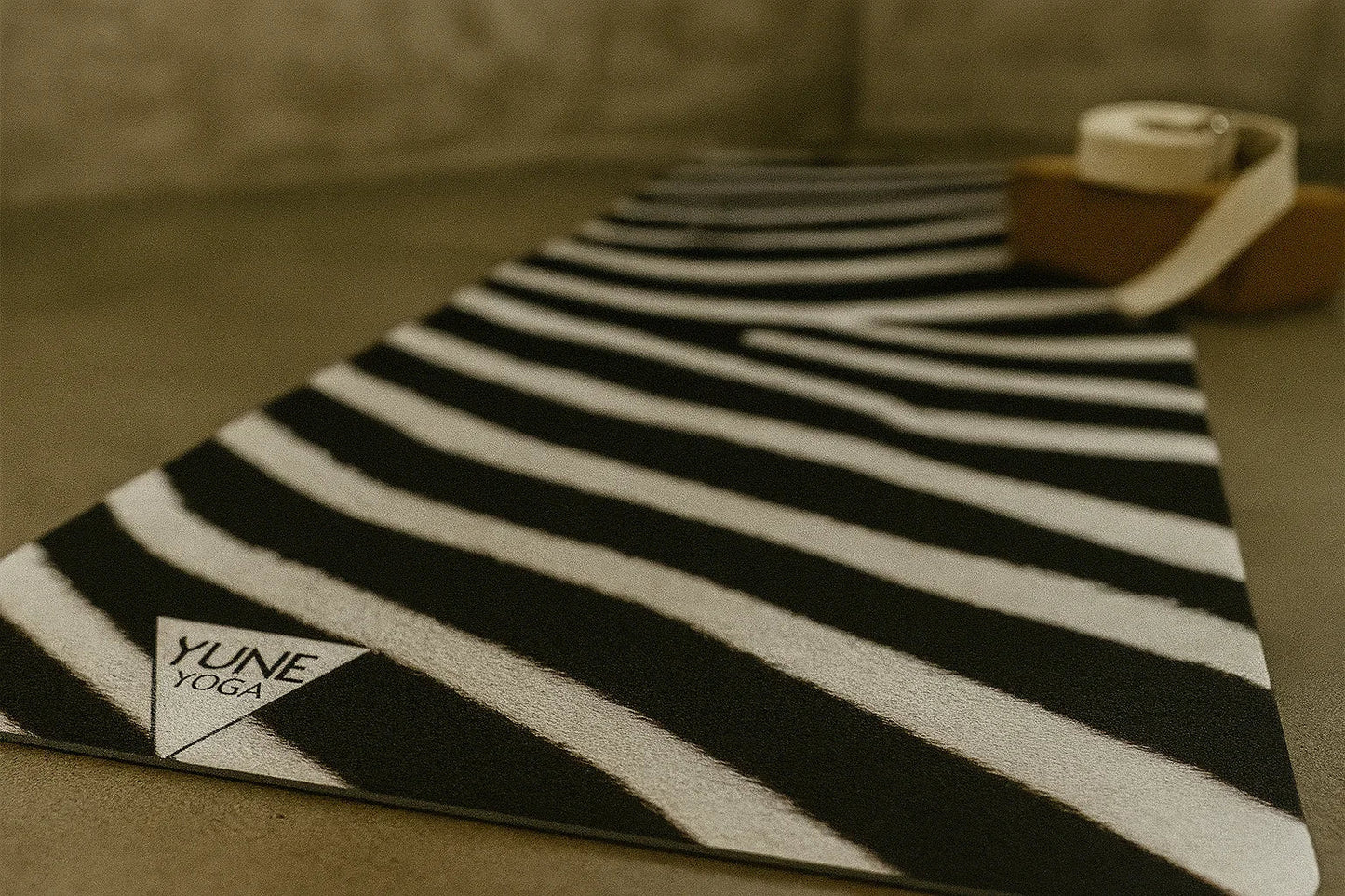 Black and white striped yoga mat with 'Yune Yoga' logo on a brown surface